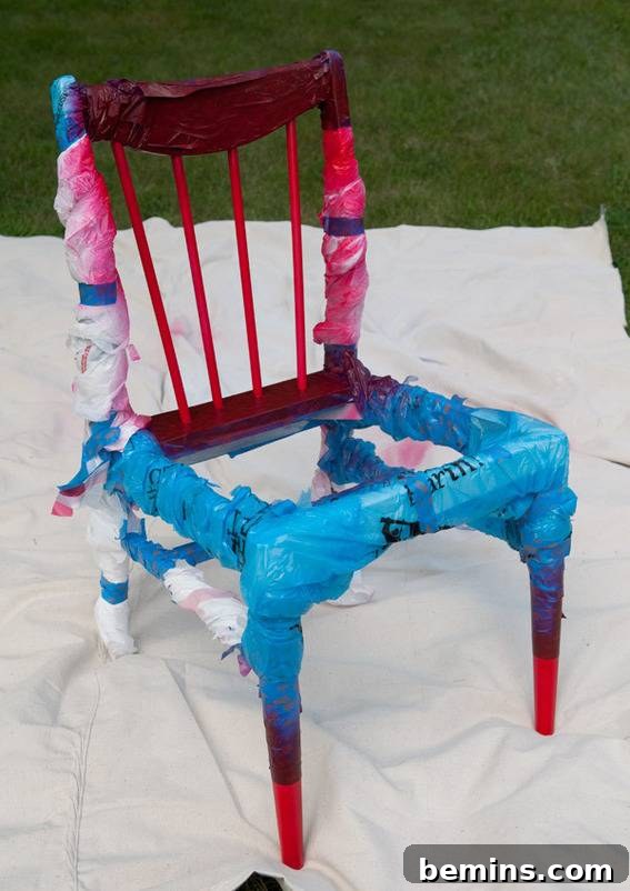 Wooden chair wrapped with cloth ribbons on top of drop cloth. Red painted spindles.