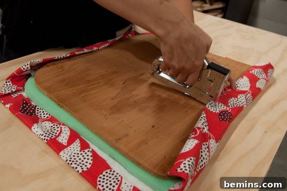 A wood board that is having cloth stapled to the front. Stapling the new fabric to the seat.