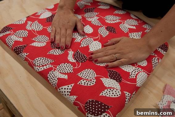 A person places both their hands on a red decorated pillow. Ensuring the corners are wrapped and taut.