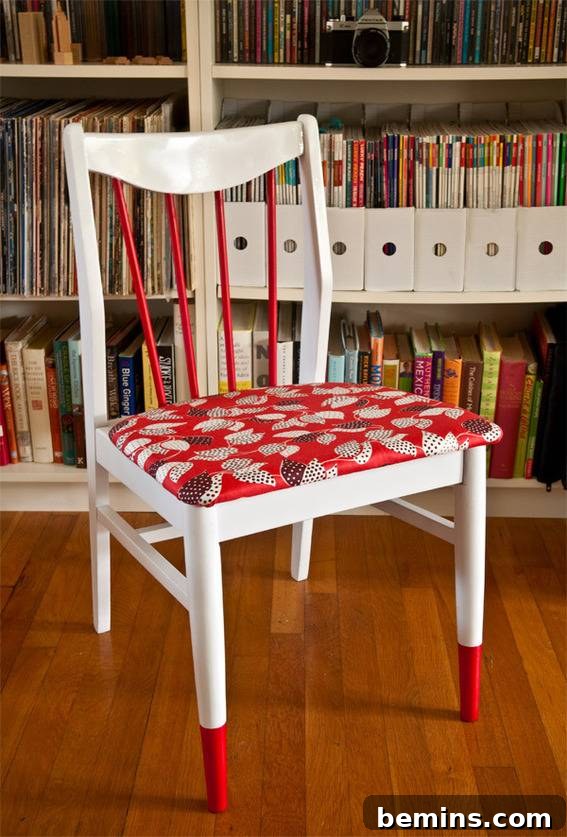 A red and white chair is in front of a large white bookcase. The completed chair makeover.