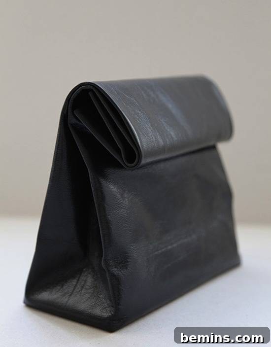 Leathercraft Dreams: 11 DIY Projects to Ignite Your Creativity 8 A black leather bag which is shaped like a lunch bag is folded down and seen from an angle on a white table and beige wall behind.