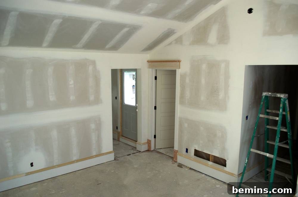 A green ladder stands in the doorway of an unfinished room, with new sheetrock installed, signifying construction progress.