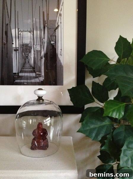 How to Craft Your Own Charming Miniature Cloche 4 A little brown statue under a glass cover on a table with a marine photo hanging above it.
