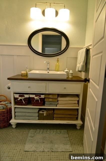 Bathroom counter with towels folded underneath beneath an oval mirror in a bathroom, revealing a stylish repurposed cabinet vanity.