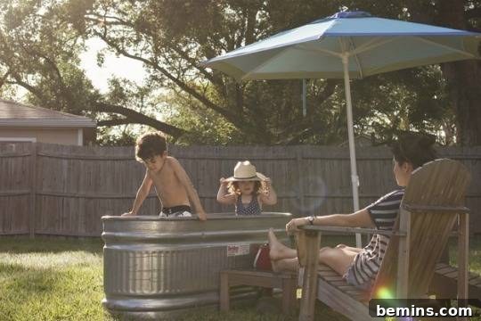 Two children are playing in an oval basin outside, demonstrating a galvanized steel livestock tank repurposed as a tub.