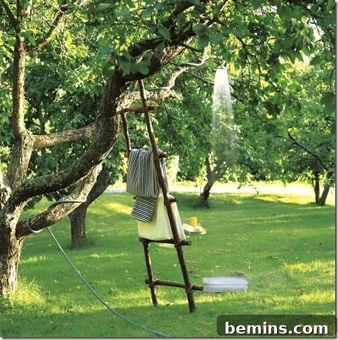 A flimsy ladder holding towels leans against a tree, complementing a charming DIY outdoor shower setup.