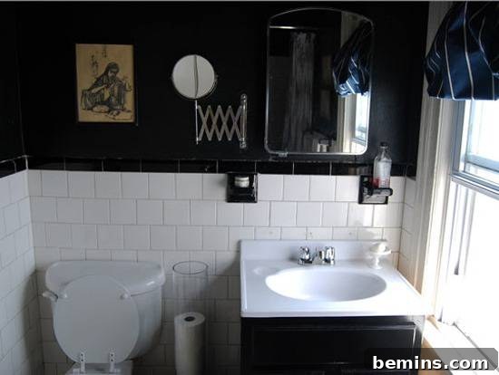 Dark Indulgence: 10 Bathrooms Embracing the Moody Palette 8 A black and white bathroom with half black walls and half white tile, creating a chic and modern look.