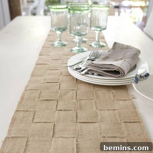 Plates, cloth napkins, forks and wine glasses sit on top of a white table with a tan runner.