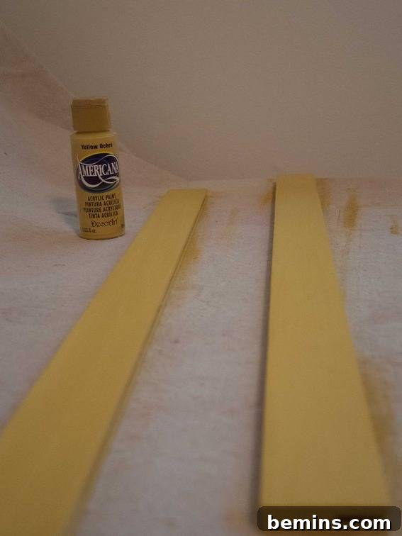 A bottle of paint positioned near two wooden slats, showcasing the materials used in the DIY poster hanger project.