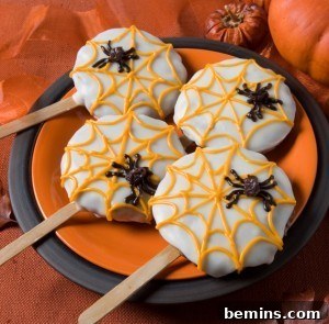 Spiderweb cookies with spiders and popsicle sticks on a plate.
