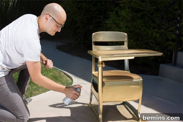 A man spray painting an old wooden school desk.