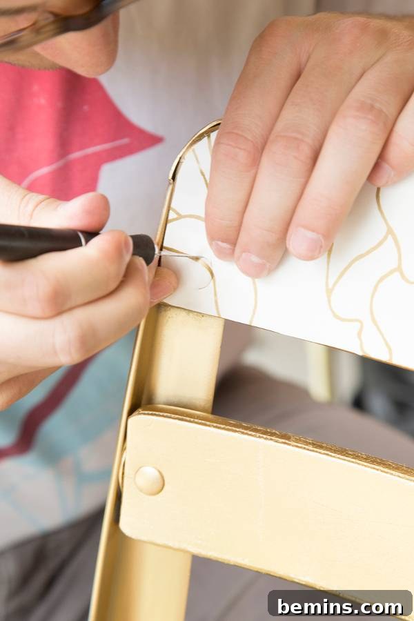 A person's hand drawing on the back of a beige chair.