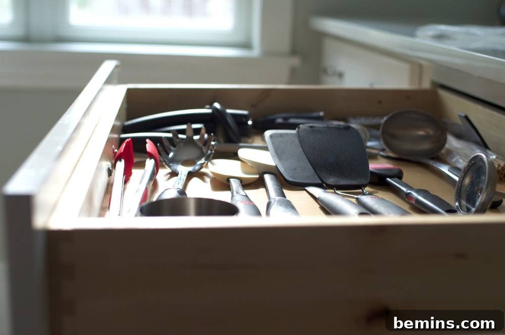A kitchen drawer is open and exposes all of the tongs, spatulas, spoons and measuring cups inside.