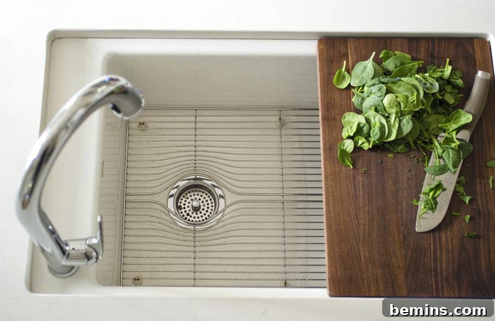 A knife and some green leaves sitting on a wooden cutting board that is over a sink.