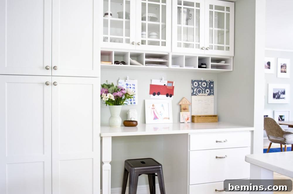 A white kitchen with a built in desk that has a black stool under it.