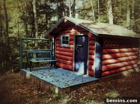 A red log cabin in the woods with a blue porch surrounded by trees