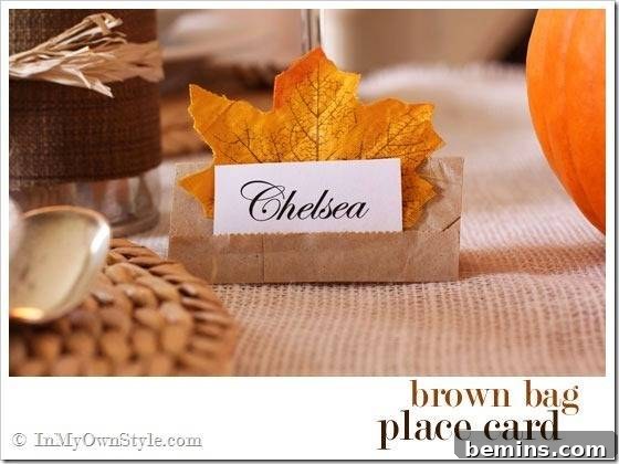 A place card is backed by a maple leaf and held by a folded brown piece of paper.