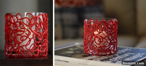 DIY Holiday Votive Candles with Hot Glue Designs 6 A lit tea candle inside of a glass cup covered in a swirly red design, showcasing the finished DIY hot glue candle holder with a candle.