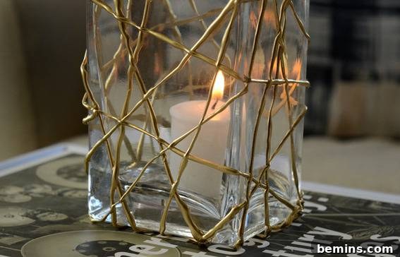 DIY Holiday Votive Candles with Hot Glue Designs 7 A lit tea candle in a tall rectangular vase with criss crossed gold lines on the outside, displaying a geometric hot glue design.