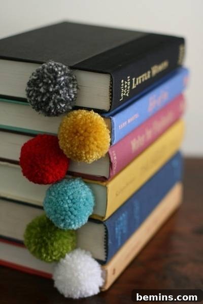 10 Ways to Add Pom-Pom Power to Your Decor & Crafts 11 Pom-pom bookmark visible on the pages of a stack of books, a perfect gift for book lovers.