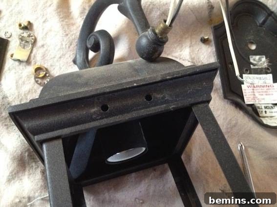 Metal lantern with a handle near pile of screws on a fabric surface. Illustrates the removed hardware from the lantern.