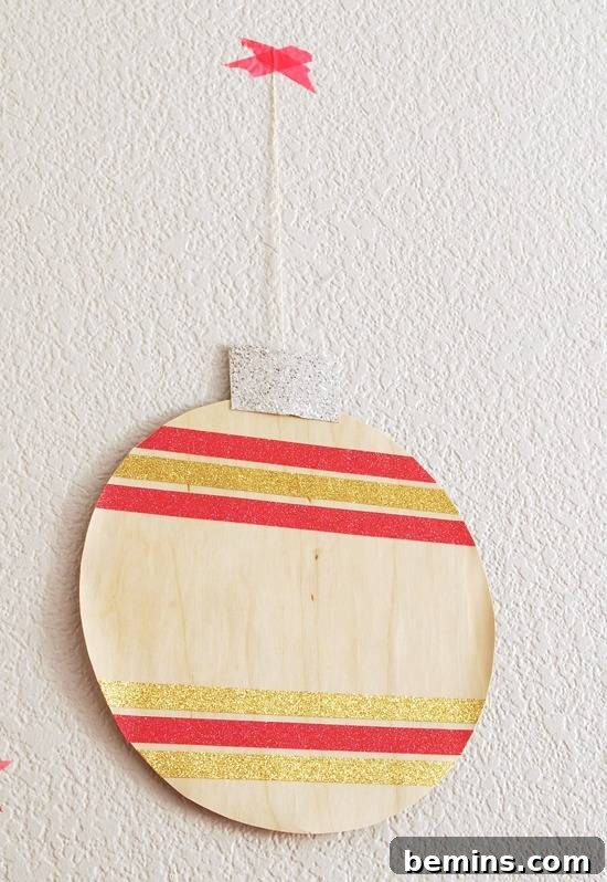 Flat, round hanging Christmas ornament featuring gold and red stripes on pale wood.