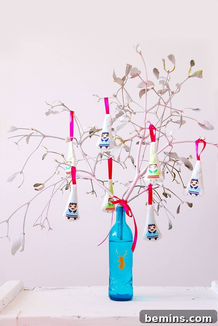 Triangle shape papers with people painted on them are strung with ribbon as ornaments on a tree made of branches