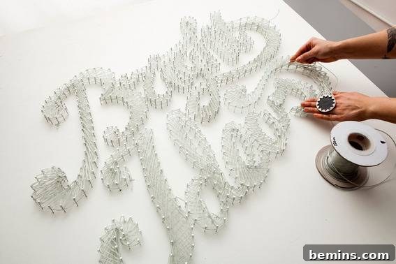 How to Craft a Glowing Typographic Display 3 A hand demonstrates how to wrap neon EL wire around nails to create a typographic sign.