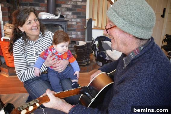 A heartwarming scene of a person playing guitar while a woman and baby happily enjoy the music in their renovated coastal cottage.