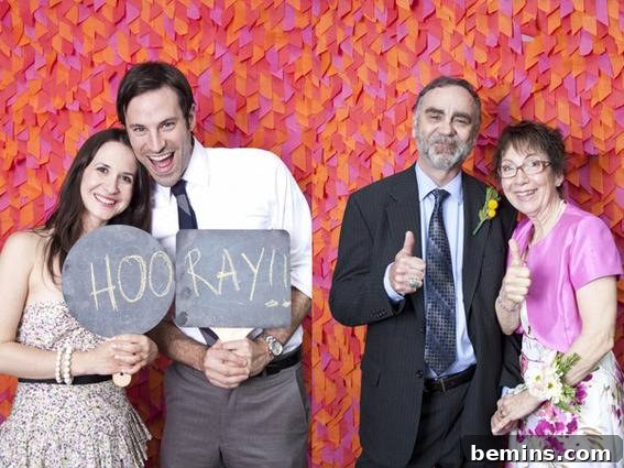 A man and woman hold up a sign that says hooray in front of a confetti backdrop, next to an older couple holding up thumbs