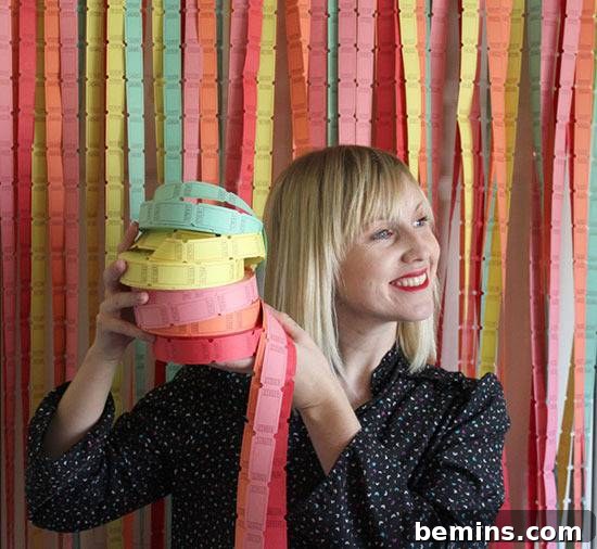 A blonde woman smiling hold a stack of green, yellow, pink, orange and red tickets against a wall of unfurled tickets.
