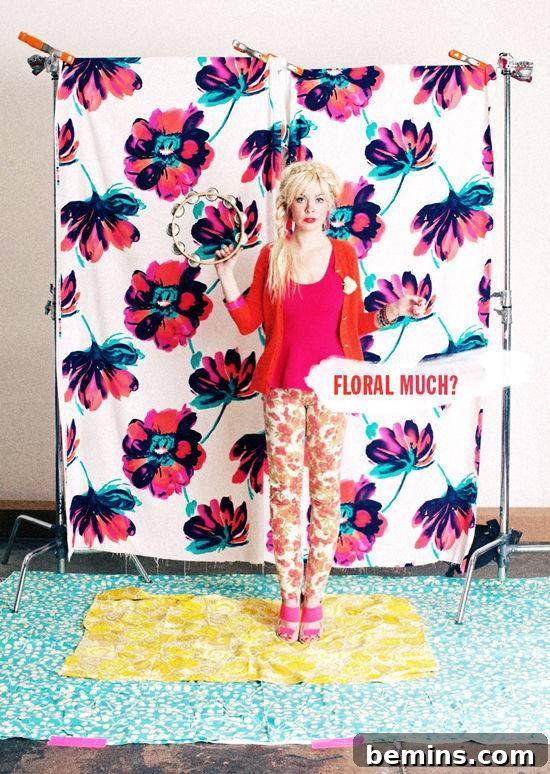 A woman wearing red top and floral pants is standing in a room where floral sheet is on her bottom and back as well.