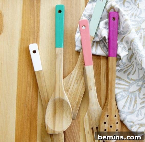 Light wooden spoons with colorful handles are on a woodsn surface.