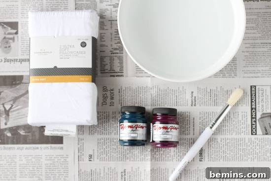 Dip-Dye Pillowcase Perfection: Achieving the Ombre Look with Ease 3 A new bundle of cloth, a white bowl of water, two small bottles of paint, and one white paintbrush all sitting on spread out newspaper.