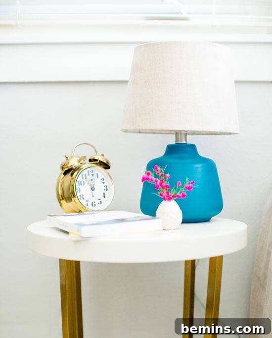 Night lamp, clock, book and flower pot is on the white wooden table.