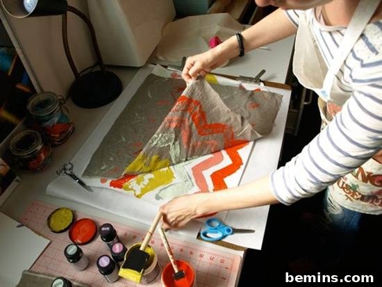 14 Textile DIYs to Level Up Your Craft Game 5 A crafter's hands working with vibrant orange and yellow paint, creating a unique monoprint design on fabric.