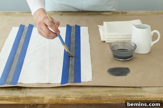 14 Textile DIYs to Level Up Your Craft Game 7 A person meticulously painting a picture in a serene setting, with a mug, glass, and cloths nearby.