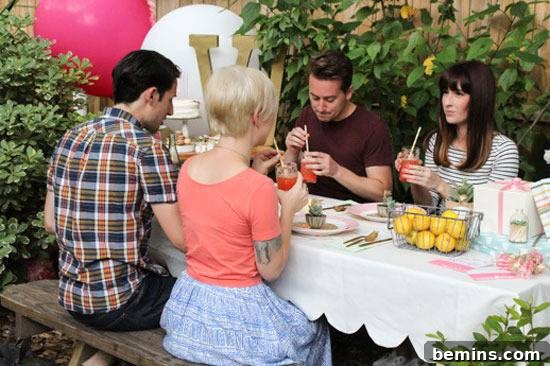 People enjoying a picnic at a table with a scalloped tablecloth and balloons.