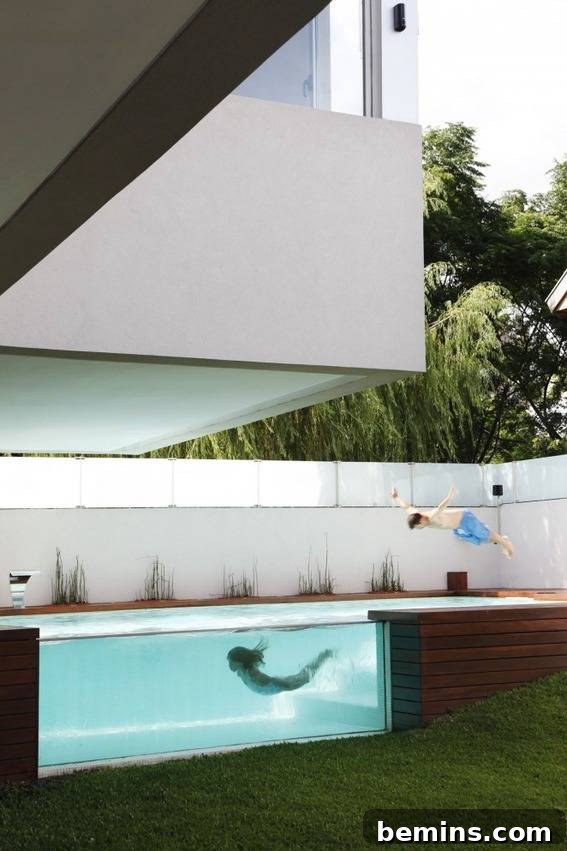 A child swims in a see through pool at a modern house.
