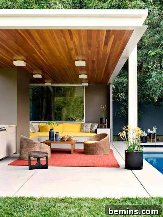 This modern patio features a wood ceiling with lighting, a large red area rug, yellow sofa, and simple wicker-looking chairs.