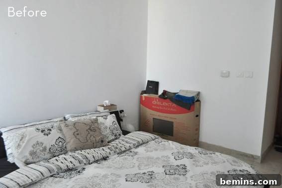 A cardboard box is being used as a bedside table in a white room.