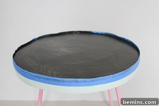 A round stool has a black top and pink legs.