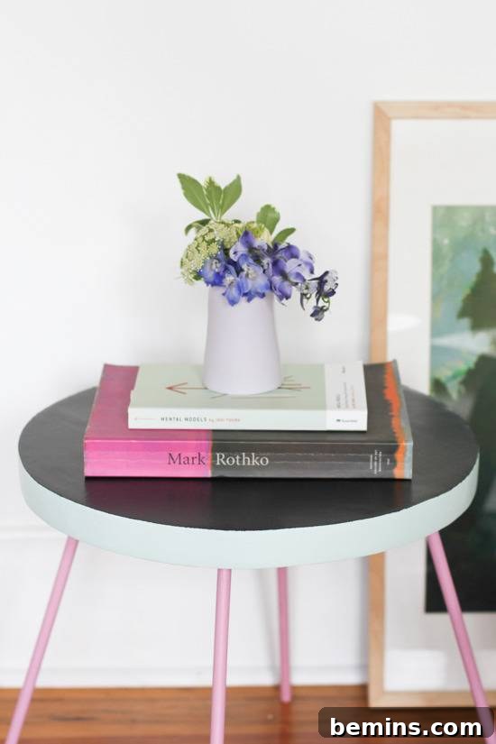 A small round table has a black top and pink legs.