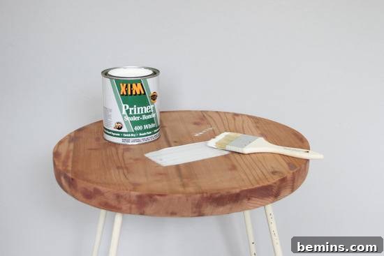A can of primer and a paintbrush sit on a round chair.