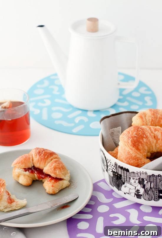 A croissant on a plate with a knife, a drink, and trivets with croissants.