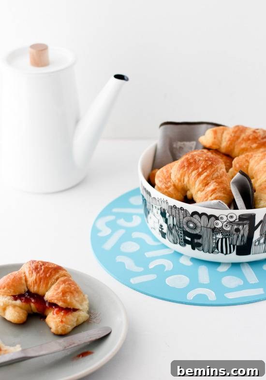 Croissant cut in half with jam, and a bowl of croissants.