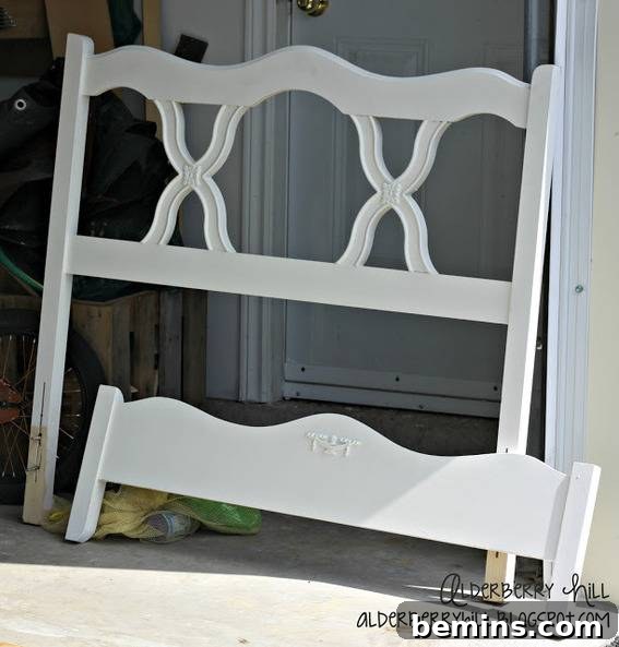 A white bed end leans against a wall by a doorway.