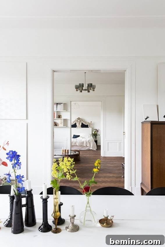 Blue and green flowers adorn a kitchen counter overlooking the living room, with a glimpse of a bedroom and bed through an open door.