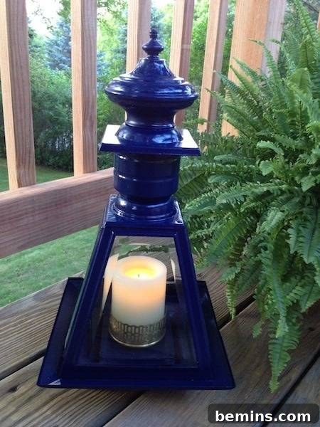 A dark blue shiny pagoda tea candle holder on a wooden deck next to a fern plant, showcasing the finished lantern in its outdoor setting.