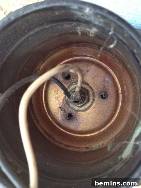 A white candle wick hangs out of rustic antique lantern, showcasing its new purpose.